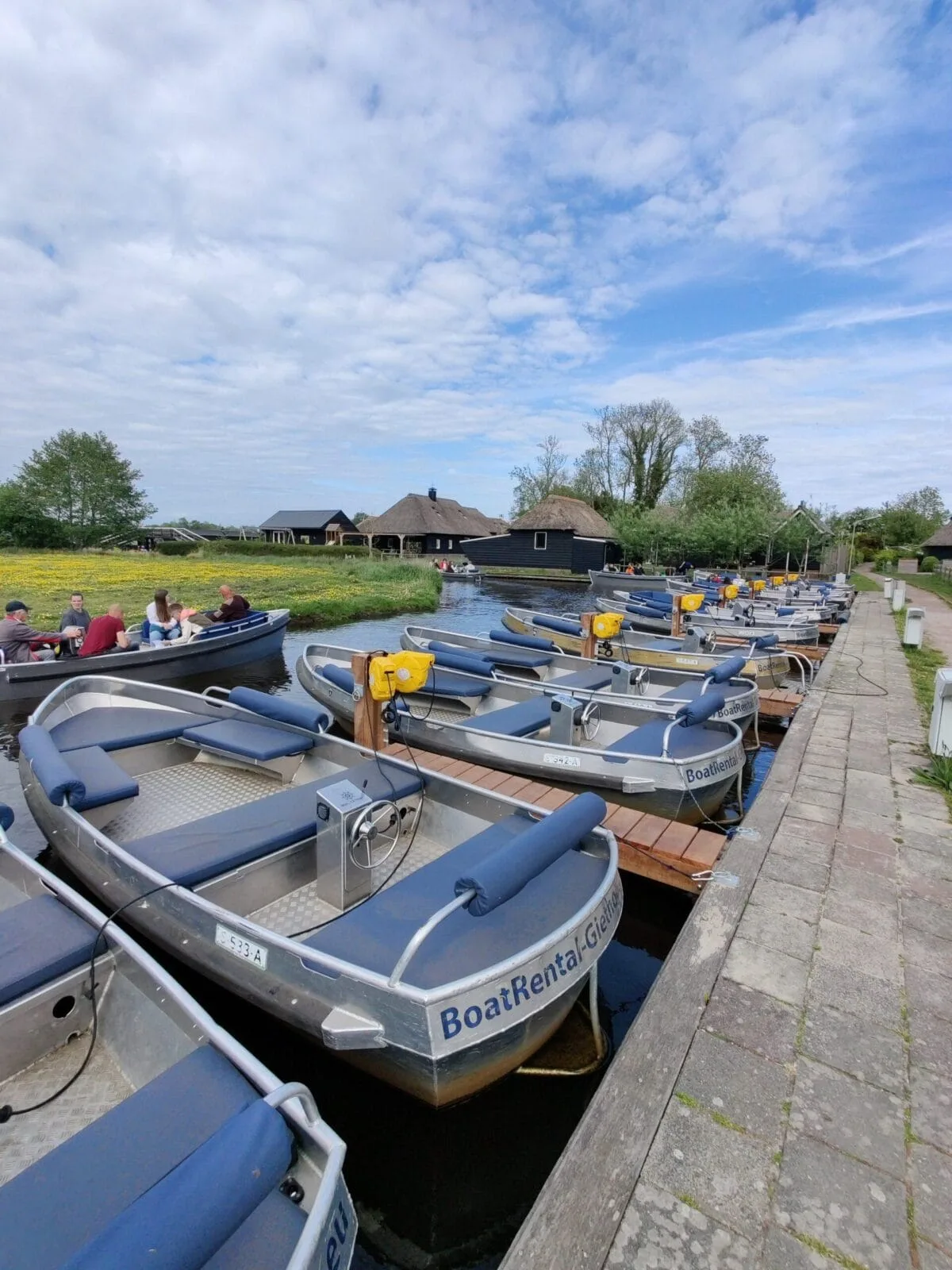 Elektrische huurboten van BoatRental Giethoorn afgemeerd aan de steiger, met gasten op het water
