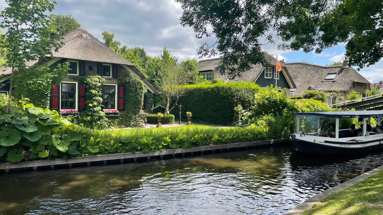 Rieten huisjes langs een gracht in Giethoorn met een rondvaartboot vol toeristen