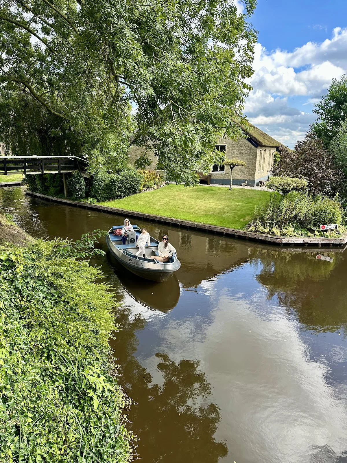 Drie mensen varen in een bootje door een rustig kanaal langs een Nederlands rietgedekt huis