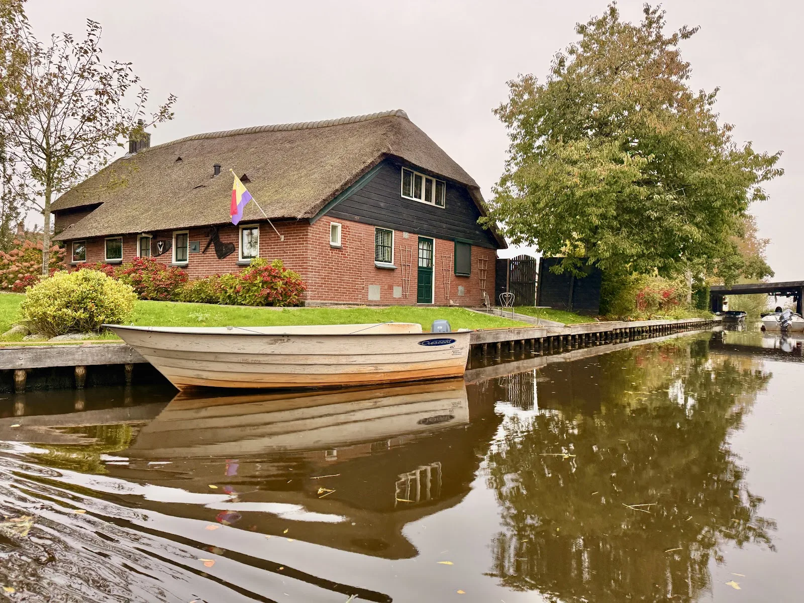 Rieten boerderij aan rustig kanaal met houten bootje en herfstkleuren in Giethoorn